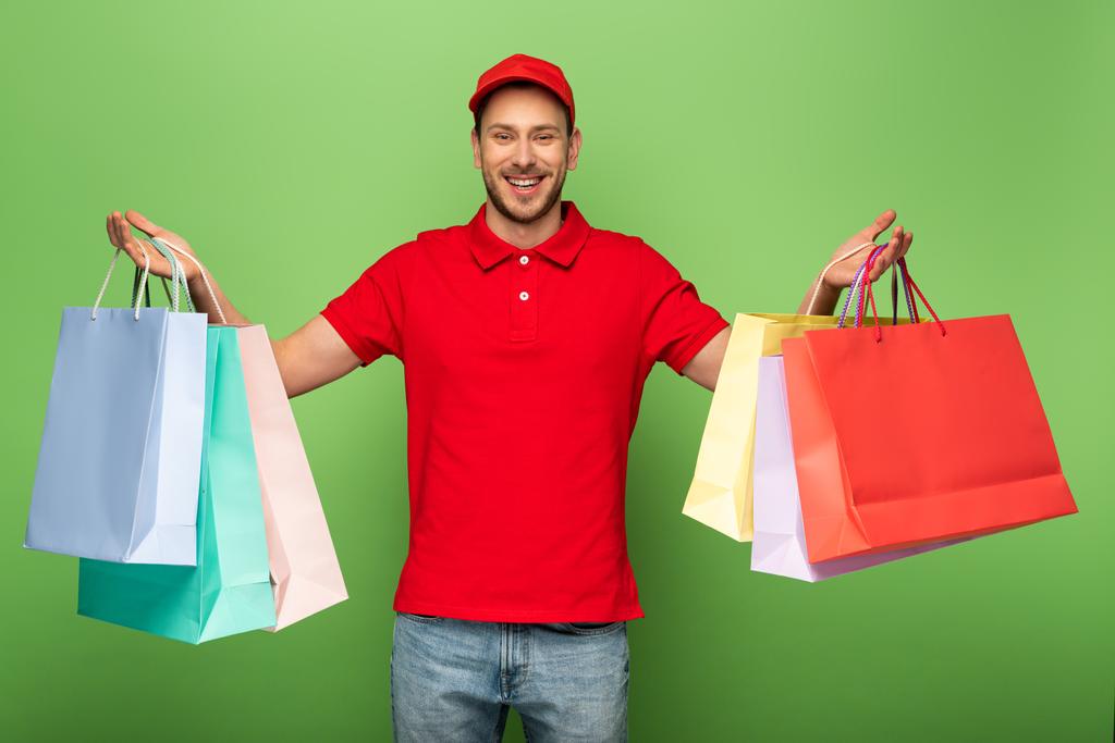 homem de entrega feliz em uniforme vermelho segurando sacos de compras no verde
 - Foto, Imagem