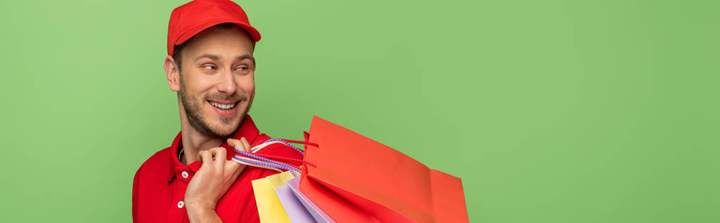 onnellinen toimitus mies punainen univormu tilalla ostoskassit eristetty vihreä, panoraama laukaus
 - Valokuva, kuva