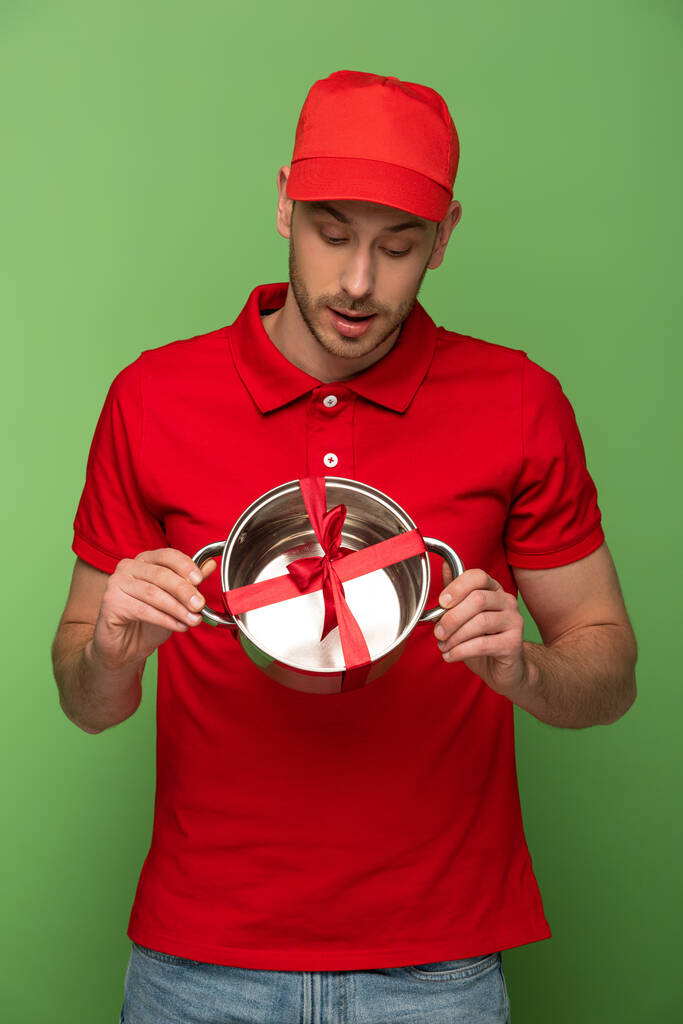 livreur en uniforme rouge tenant casserole avec arc sur vert
 - Photo, image
