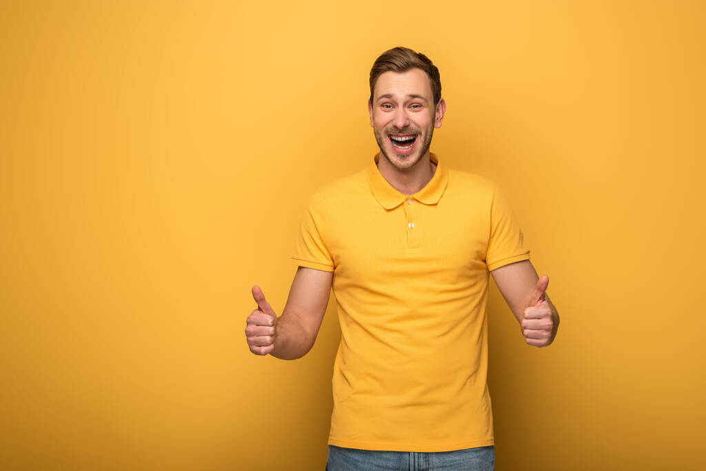 glücklich schöner Mann in gelbem Outfit zeigt Daumen nach oben auf gelbem Hintergrund - Foto, Bild