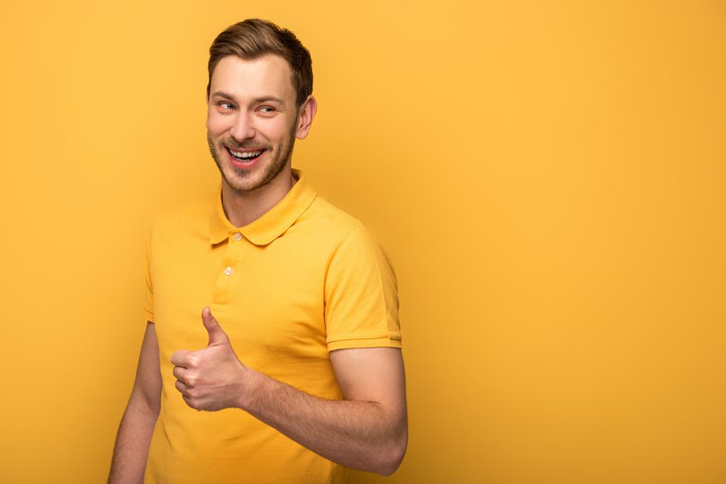 happy handsome man in yellow outfit showing thumb up on yellow background - Photo, Image