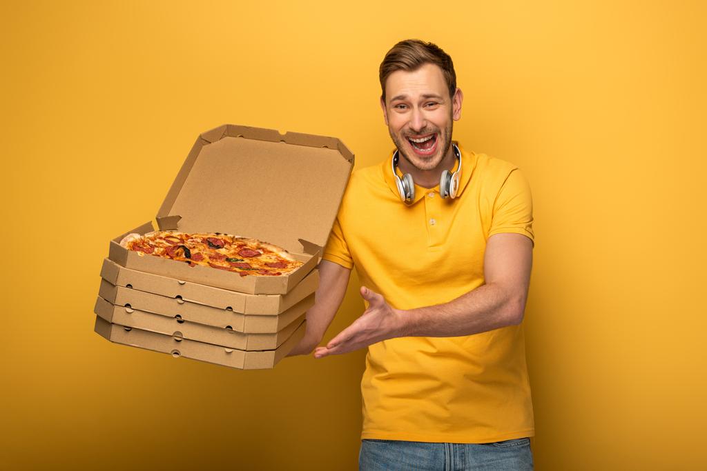 幸せな男ですヘッドフォンで黄色の背景にピザを保持 - 写真・画像