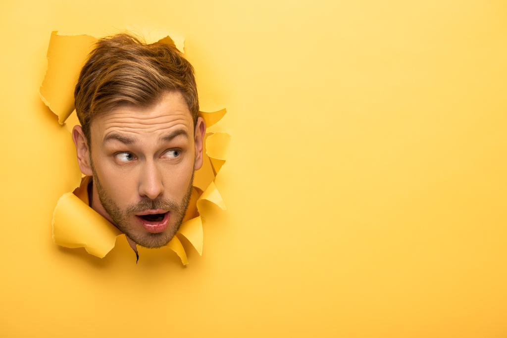 impactado hombre guapo con cabeza en agujero de papel amarillo
  - Foto, Imagen