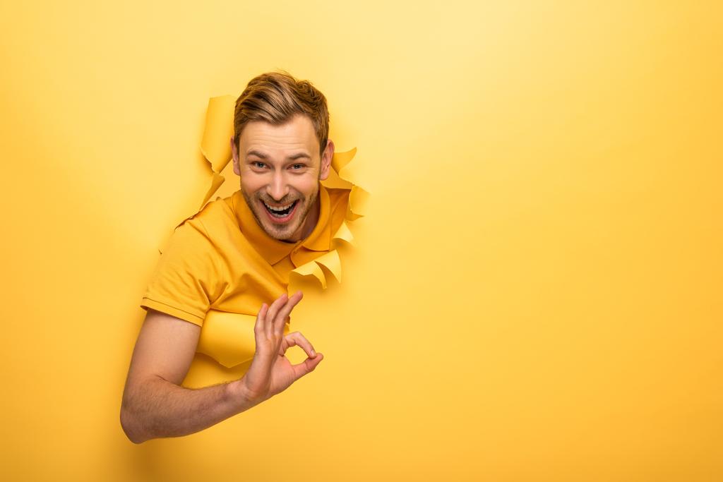 onnellinen komea mies keltainen asu keltainen paperi reikä osoittaa ok merkki
 - Valokuva, kuva