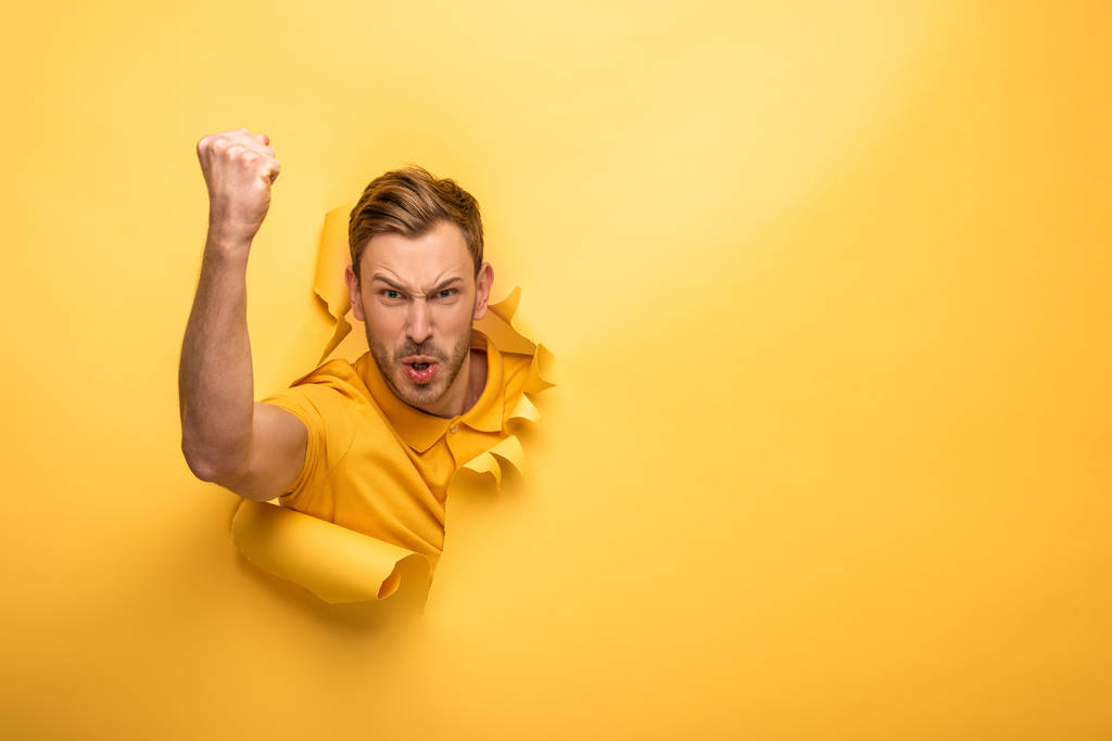 angry handsome man in yellow outfit in yellow paper hole showing fist - Photo, Image