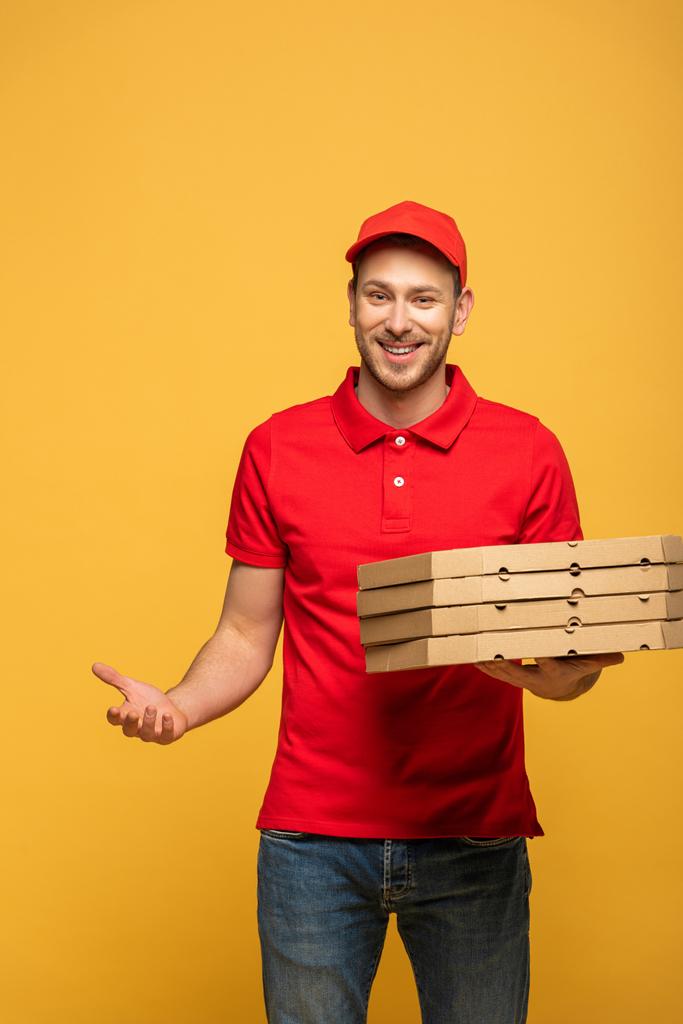 felice uomo di consegna in uniforme rossa che tiene scatole di pizza isolate sul giallo
 - Foto, immagini