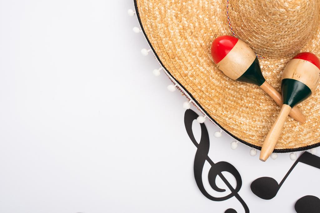Kağıt yakınındaki sombrero ve marakaların üst görünümü beyaz arkaplandaki müzik notalarını keser - Fotoğraf, Görsel