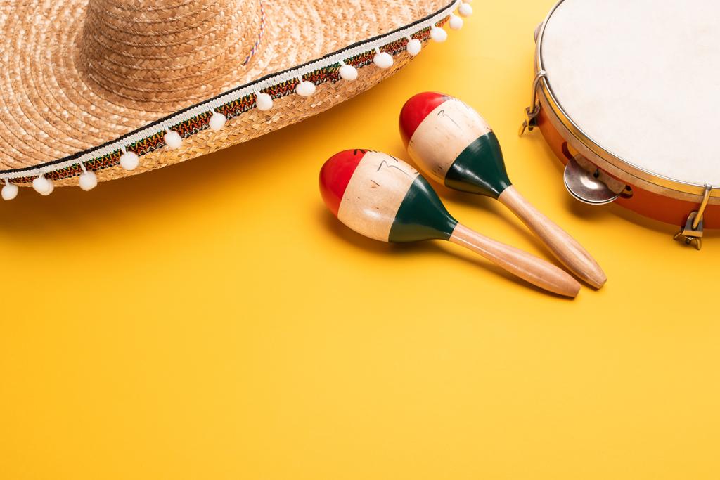 Wooden colorful maracas, tambourine and sombrero on yellow background - Photo, Image