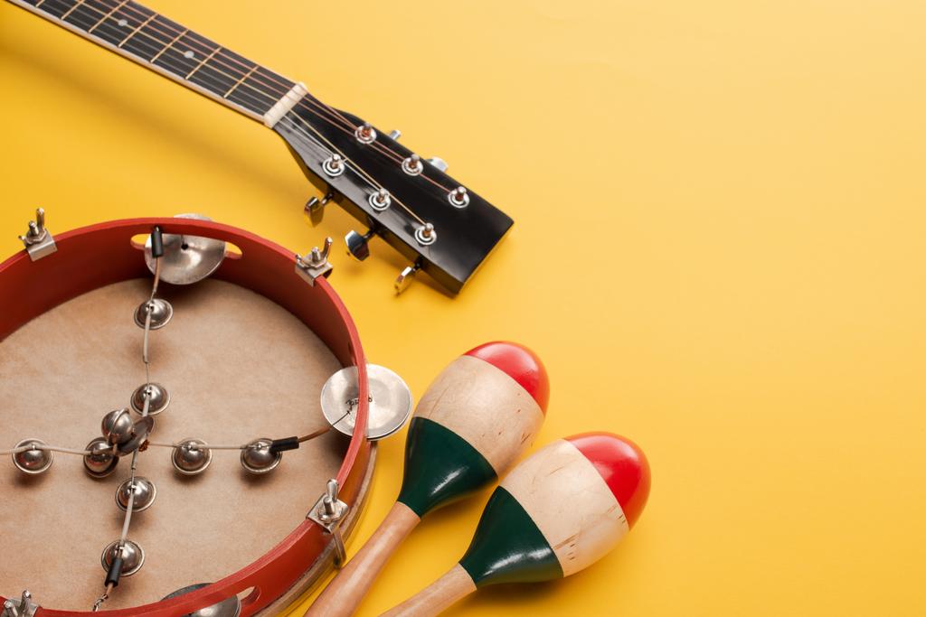 Tamburin in der Nähe bunter Maracas aus Holz und Akustikgitarre auf gelbem Hintergrund - Foto, Bild