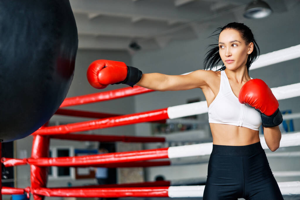 Un boxeur féminin frappe un énorme sac de boxe au gymnase de fitness. Femme pratiquant ses coups dans un studio de boxe
                     - Photo, image