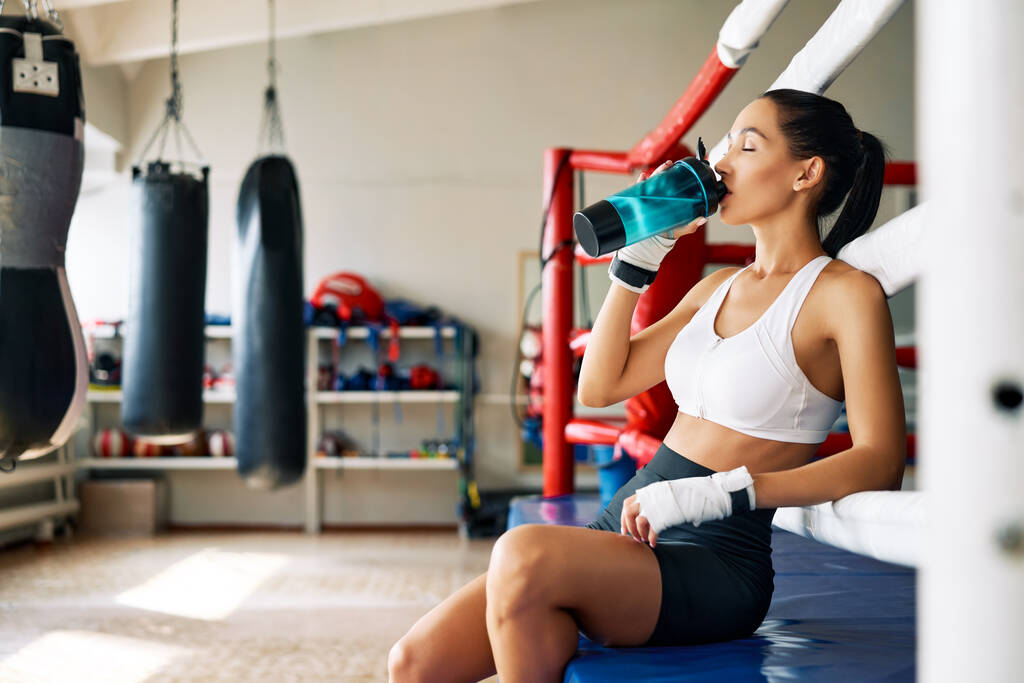 Młoda sportowa kobieta pijąca wodę po walce lub treningu na ringu bokserskim. Koncepcja sportu                                - Zdjęcie, obraz