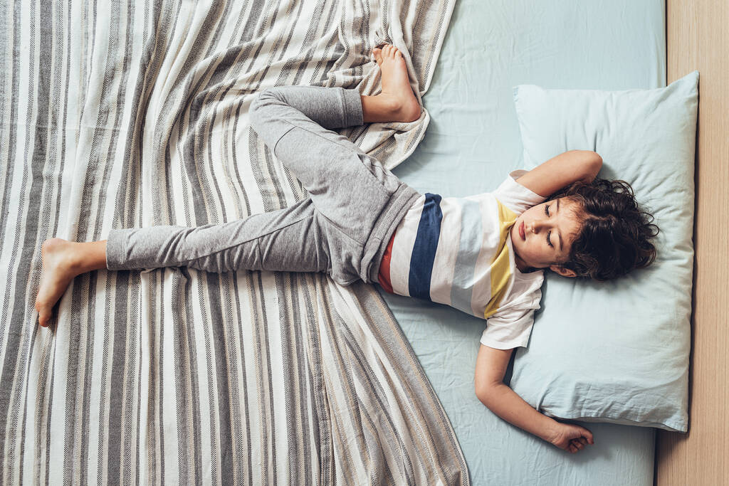 κορυφαία άποψη ενός αξιολάτρευτου μικρού κοριτσιού που απλώνεται στο κρεβάτι το πρωί όταν μόλις ξύπνησε, ευτυχισμένη παιδική ηλικία και υγιή έννοια ανάπαυσης - Φωτογραφία, εικόνα