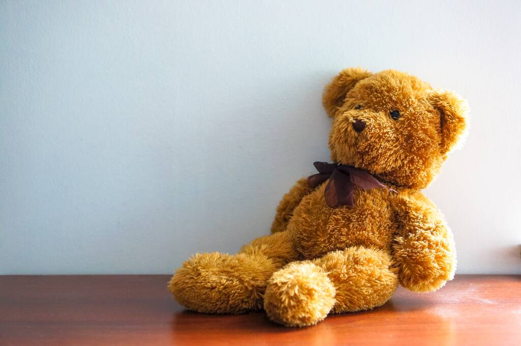 Bruine zachte teddybeer zittend op een houten ondergrond tegen een muur. - Foto, afbeelding