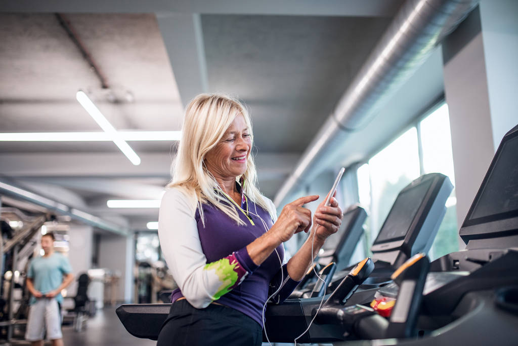 Une femme âgée avec smartphone dans la salle de gym faire de l'exercice cardio
. - Photo, image