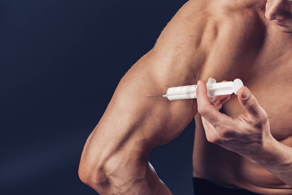 Bodybuilder maakt injectie van vitaminen. Foto van sportieve man met perfecte lichaamsbouw op donkere achtergrond. Sterkte en motivatie - Foto, afbeelding