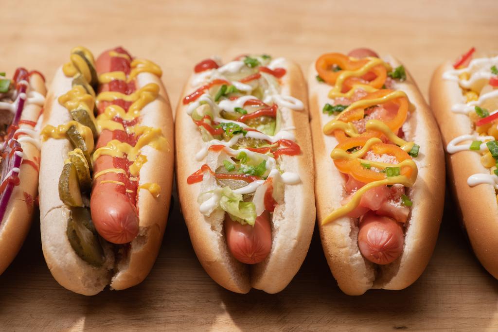 świeże pyszne hot dogi z sosami na drewnianym stole - Zdjęcie, obraz