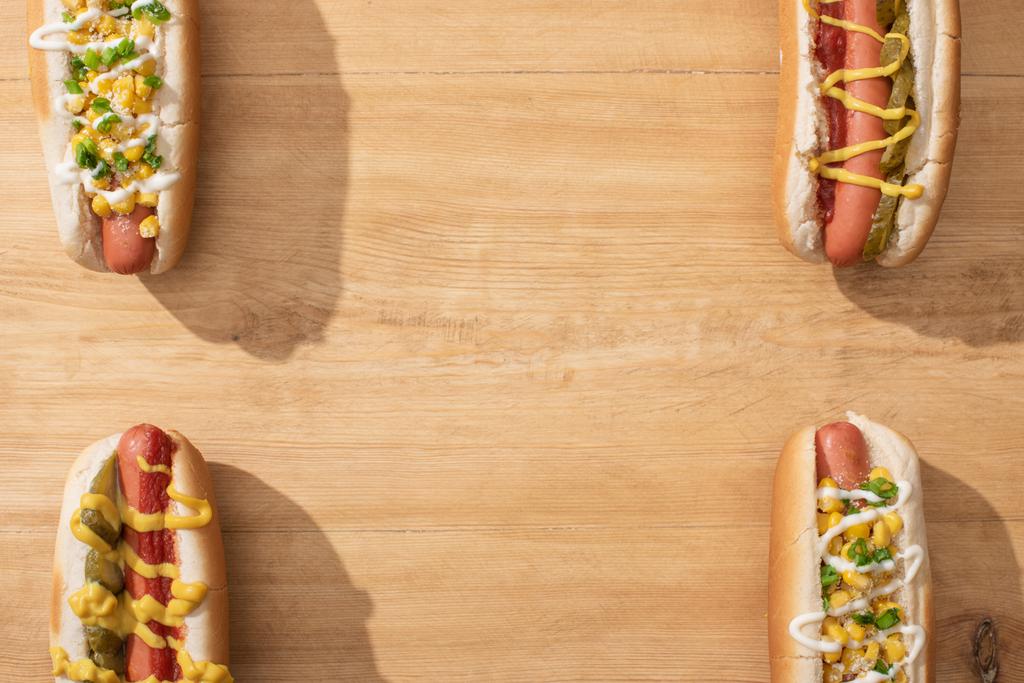 top view of delicious hot dogs with corn, green onion and pickles on wooden table - Photo, Image