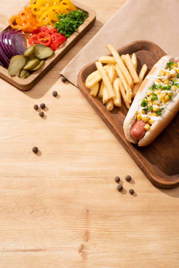 pyszne hot dogi w pobliżu pokładzie z krojone warzywa i frytki na drewnianym stole - Zdjęcie, obraz
