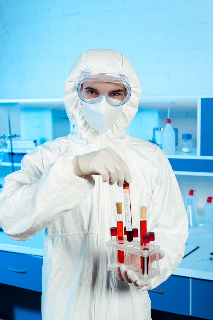 vědec v ochranném obleku a latexových rukavicích drží zkumavku s nápisem  - Fotografie, Obrázek