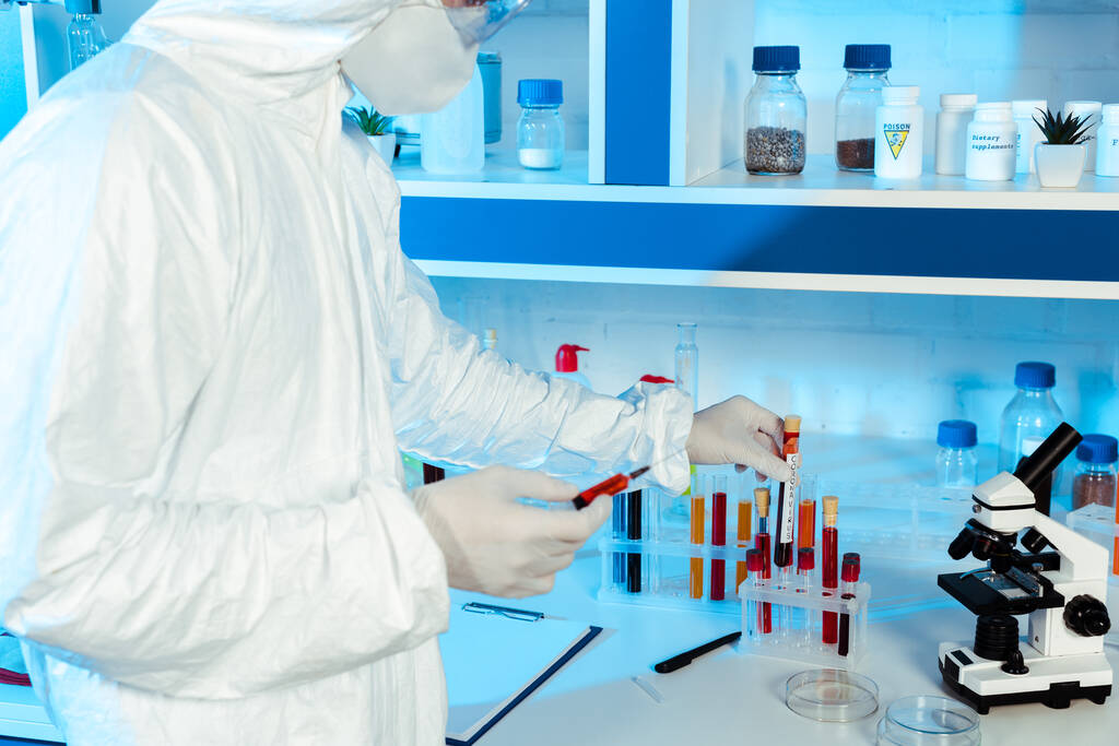 przycięty widok naukowca w rękawiczkach lateksowych trzymającego strzykawkę i probówkę z napisem koronawirusowym  - Zdjęcie, obraz