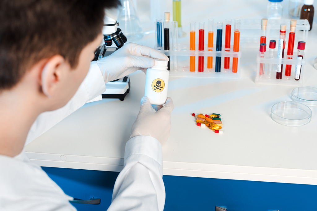 селективный фокус ученого в латексных перчатках, держащих бутылку с опасным знаком возле таблеток
  - Фото, изображение