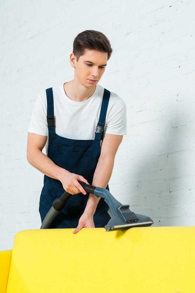 handsome cleaner removing dust on sofa with vacuum cleaner  - Photo, Image