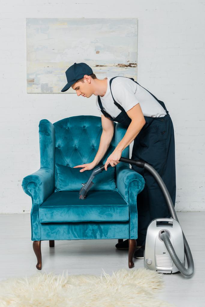 боковой вид уборщицы в мундире, моющей современное кресло с помощью вакуумной чистки
  - Фото, изображение