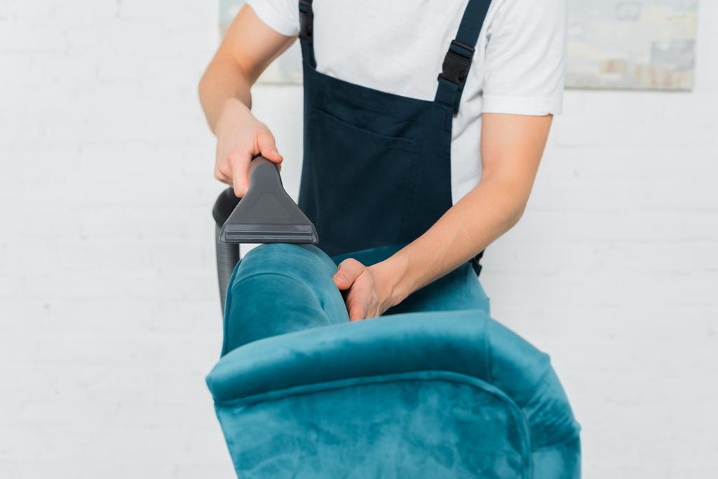 cropped view of cleaner in overalls dry cleaning modern armchair with vacuum cleaner  - Photo, Image