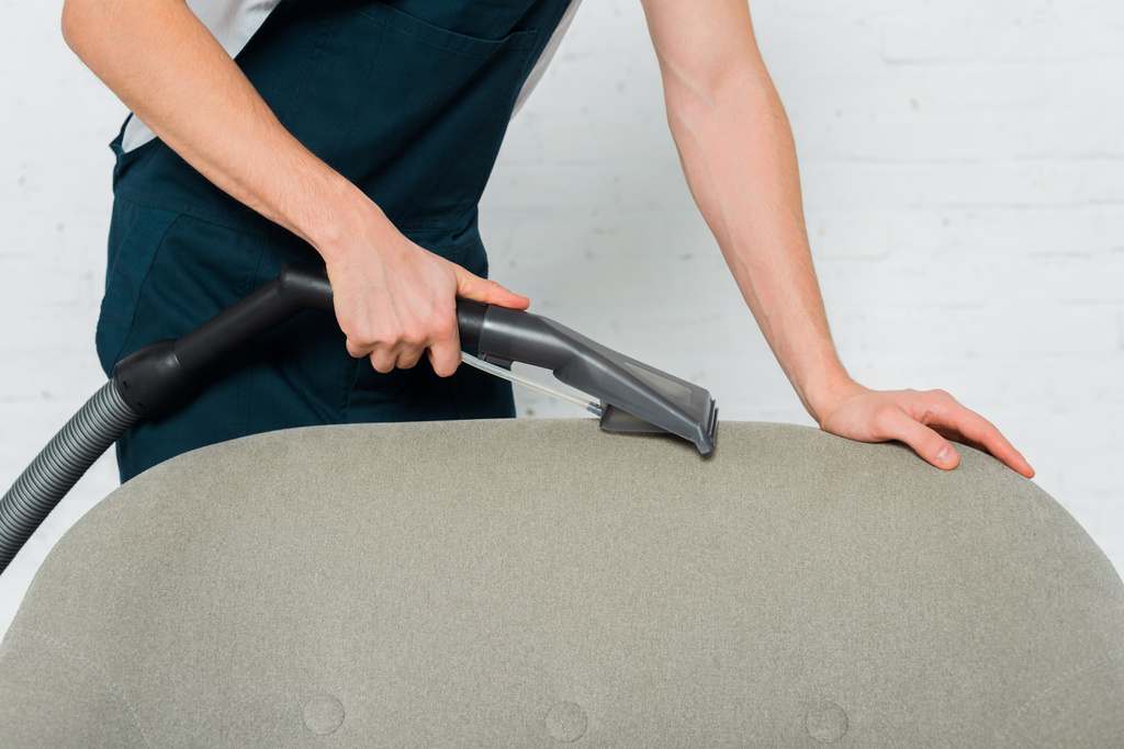 bijgesneden weergave van jonge schoner chemisch reinigen fauteuil met moderne stofzuiger  - Foto, afbeelding