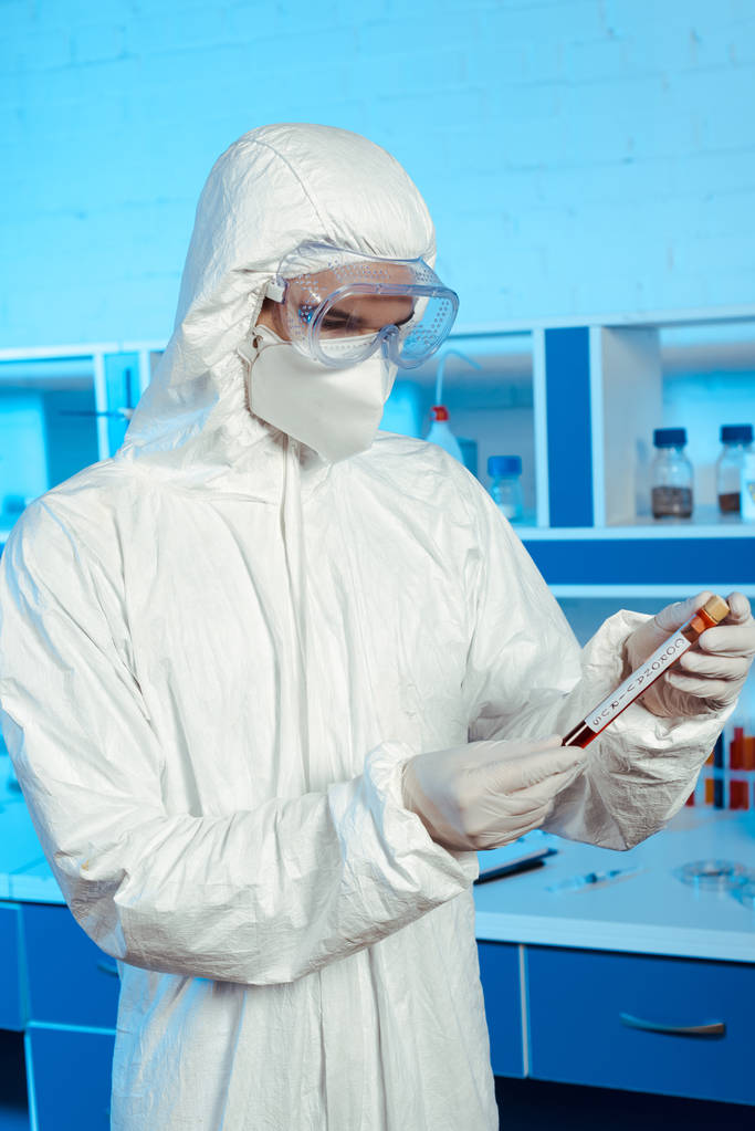 wetenschapper in hazmat pak en bril houden reageerbuis met coronavirus belettering  - Foto, afbeelding