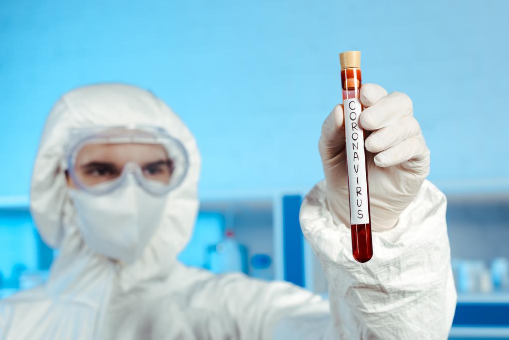 selectieve focus van wetenschapper in hazmat pak, medisch masker en bril houden reageerbuis met coronavirus belettering  - Foto, afbeelding