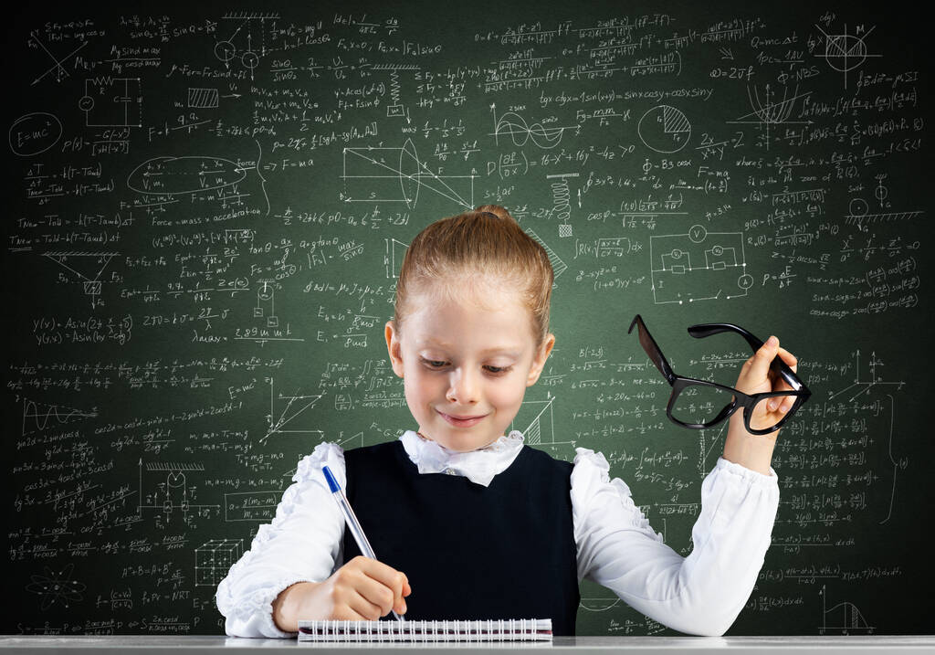 Petite fille souriante en tenue scolaire faisant ses devoirs. Il est temps d'étudier le concept. Joyeux écolière avec des lunettes assis au bureau et écrit dans un cahier. Recherche et éducation à l'école primaire. - Photo, image