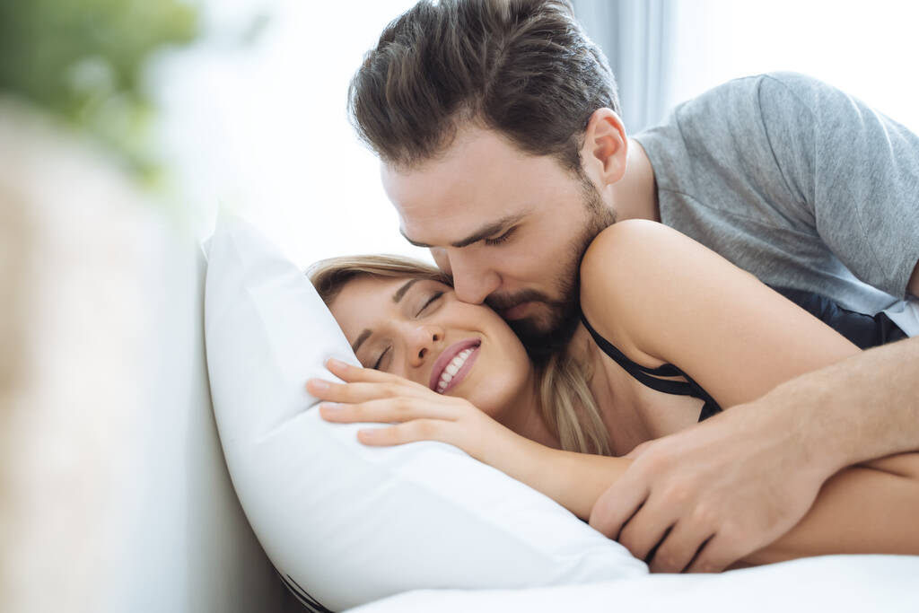Casal jovem beijando bochecha na cama acordar de manhã. casal amoroso no quarto
 - Foto, Imagem