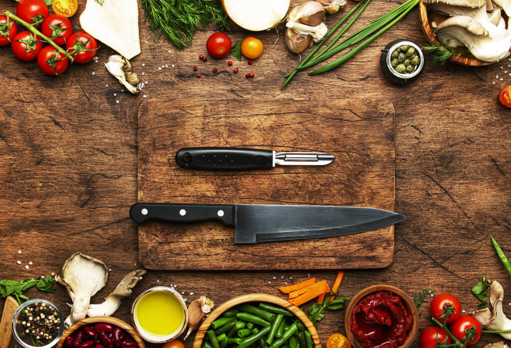 Food cooking background, ingredients for preparation vegan dishes, vegetables, roots, spices, mushrooms and herbs. Cutting board, chef knife, vegetable peeler.. Healthy food concept. Rustic wooden table, top view - Photo, Image