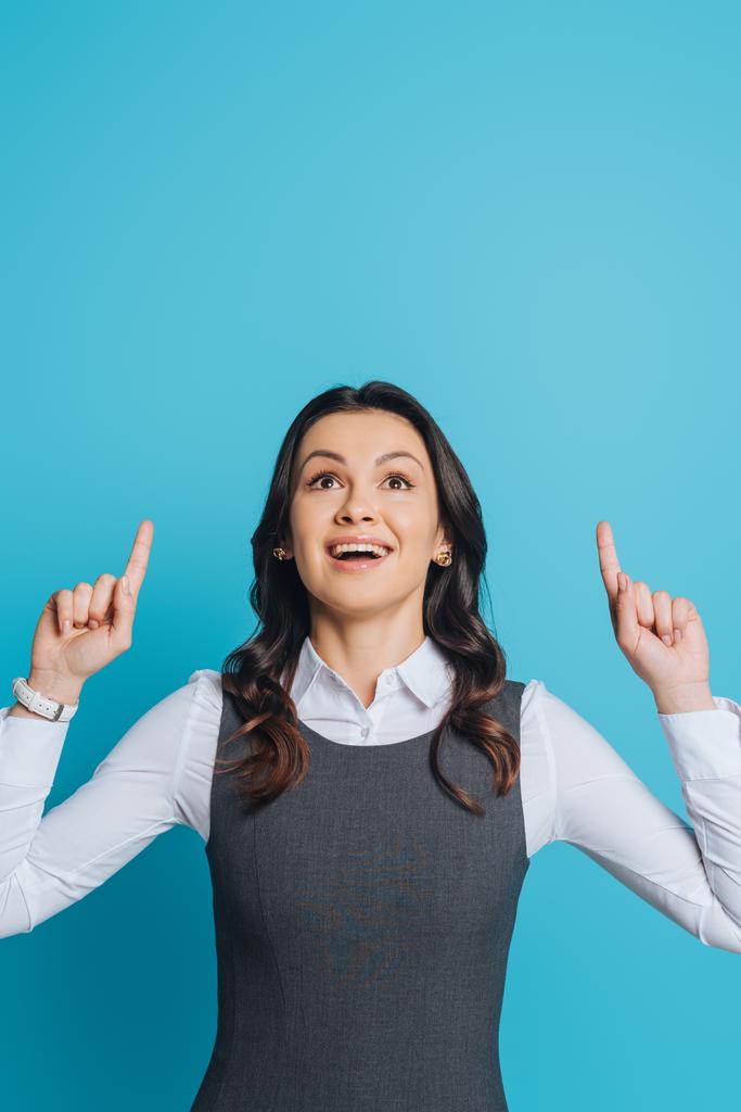 excited businesswoman looking up and pointing with fingers on blue background - Photo, Image