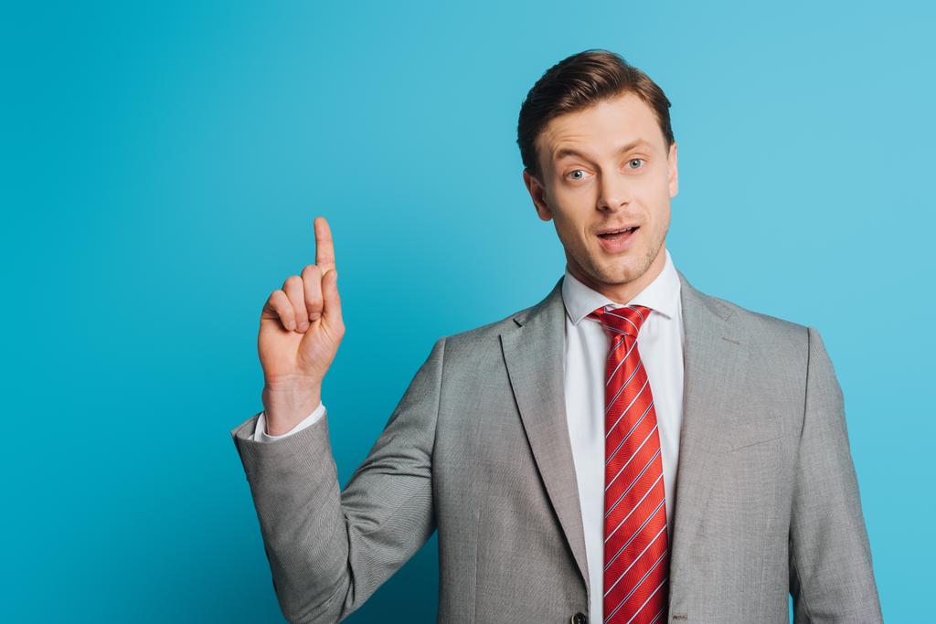 positive, handsome businessman showing idea gesture while looking at camera on blue background - Photo, Image