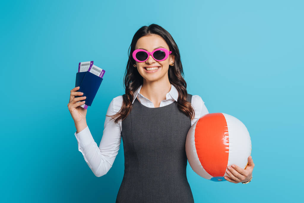 femme d'affaires souriante dans des lunettes de soleil tenant ballon gonflable, passeports et billets d'avion sur fond bleu
 - Photo, image