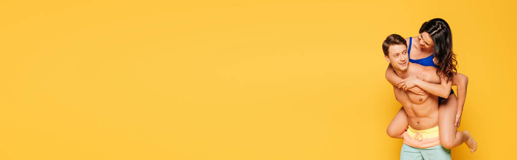 tiro panorámico de hombre sin camisa guapo piggybacking novia aislado en amarillo
 - Foto, Imagen