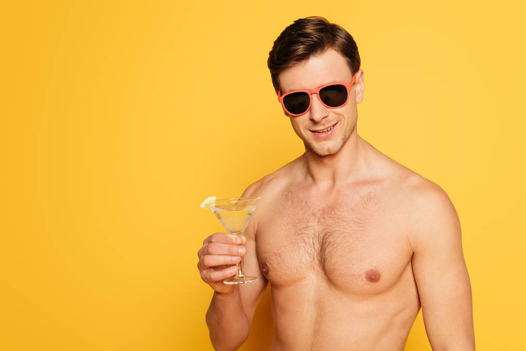 shirtless man in sunglasses holding glass of cocktail on yellow background - Photo, Image