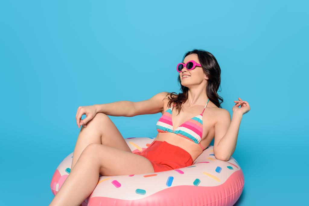 青い背景に膨脹可能なリングに座っている間にサングラスの日光浴で笑顔の女性 - 写真・画像