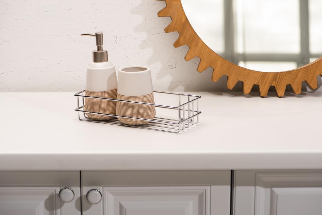 Дозатор жидкого мыла, держатель зубной щетки на полке возле круглого зеркала на стене в ванной комнате, нулевая концепция отходов
 - Фото, изображение
