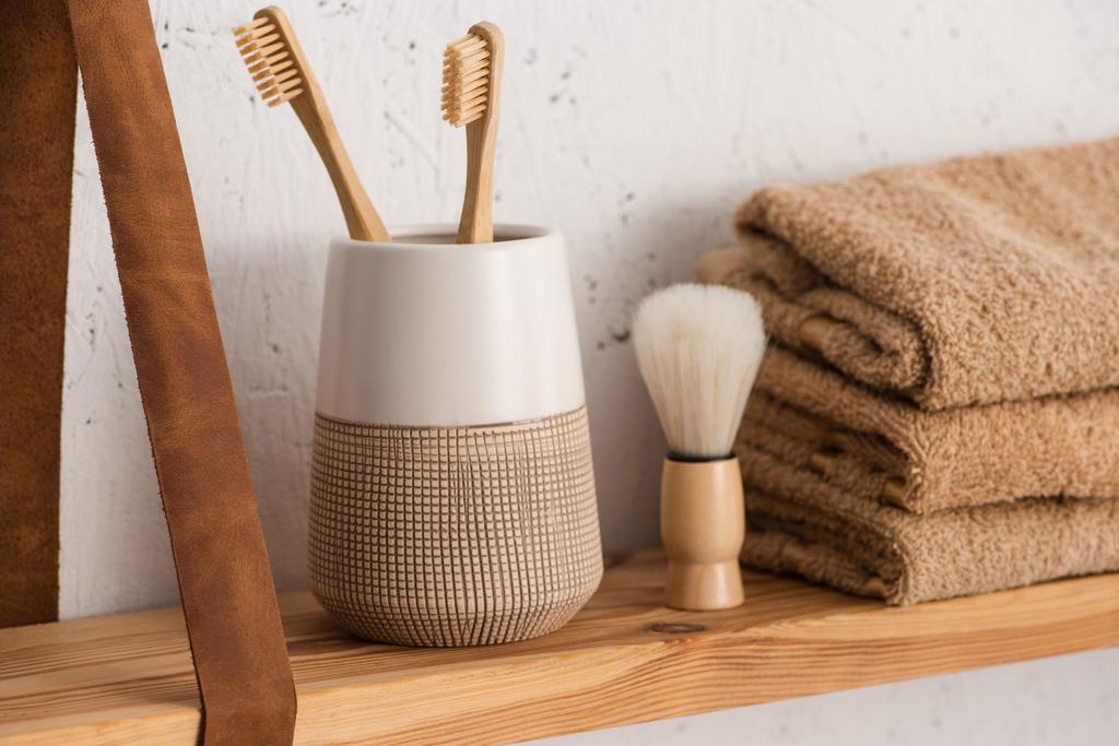 Nahaufnahme des Regals mit Zahnbürstenhalter mit Zahnbürsten, Handtüchern und Rasierbürste im Badezimmer, Zero-Waste-Konzept - Foto, Bild