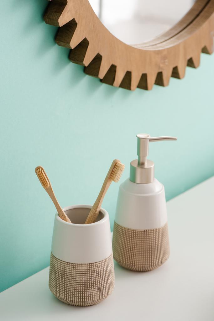Toothbrush holder with toothbrushes and liquid soap near round mirror on wall in bathroom, zero waste concept - Photo, Image