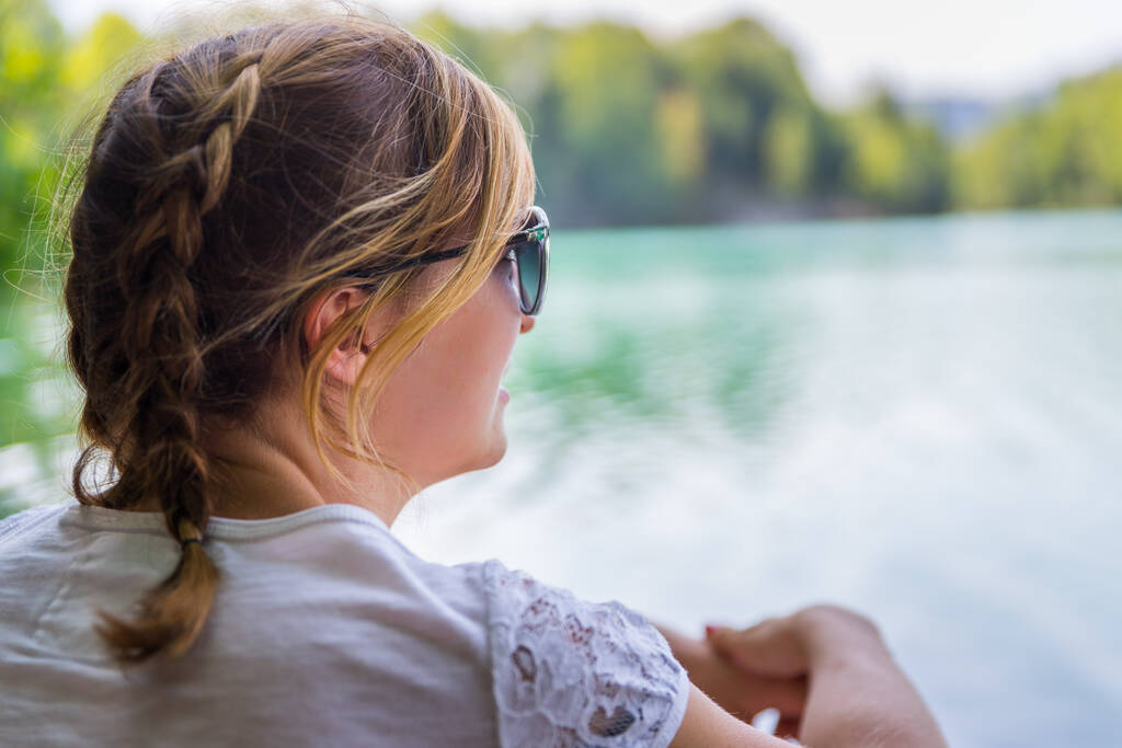 Hermosa joven está sentada junto a un lago y disfrutando del día
 - Foto, Imagen