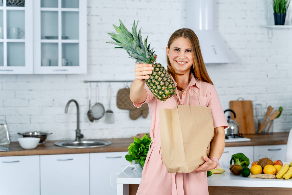 Здорова їжа вдома. Щаслива жінка показує ананас на сучасній кухні. Веганське та вегетаріанське життя
. - Фото, зображення