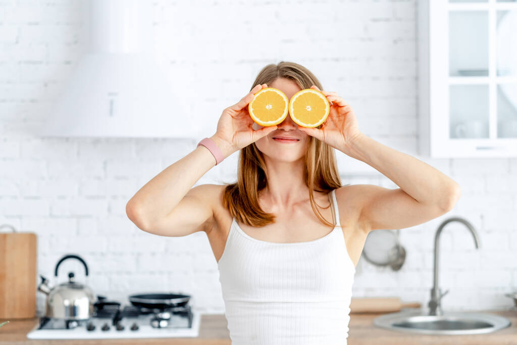 Nuori nainen valmistelee maukasta limonadia keittiössä. Detox-ruokavalio. Terveellinen ravitsemus. Oranssi puolikkaat lähellä silmiä
 - Valokuva, kuva