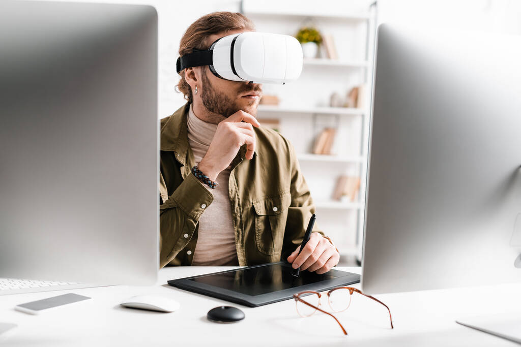 Focus sélectif de l'artiste 3D en utilisant un casque de réalité virtuelle et une tablette graphique près des ordinateurs sur la table
 - Photo, image