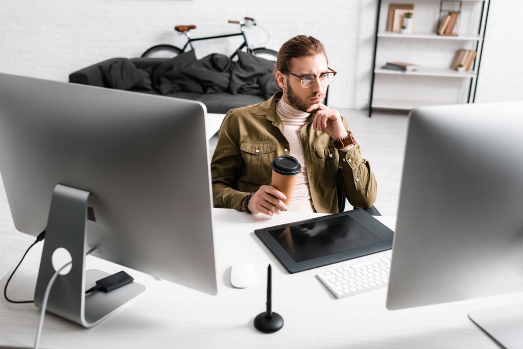 Schöner 3D-Künstler hält Kaffee in der Hand und schaut auf den Computermonitor auf dem Tisch im Büro - Foto, Bild