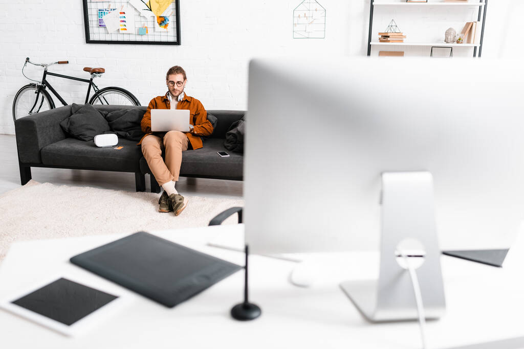 Селективный фокус цифрового дизайнера с помощью ноутбука рядом с наушниками vr и смартфона на диване в офисе
  - Фото, изображение