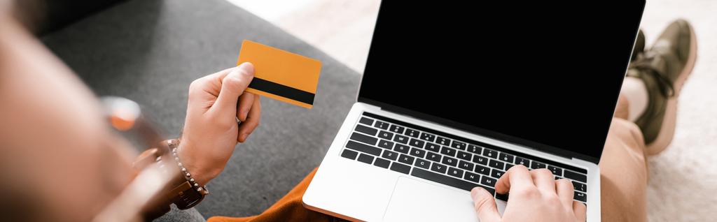 Селективный фокус цифрового дизайнера с помощью ноутбука и проведение кредитной карты на диване, панорамный снимок
 - Фото, изображение